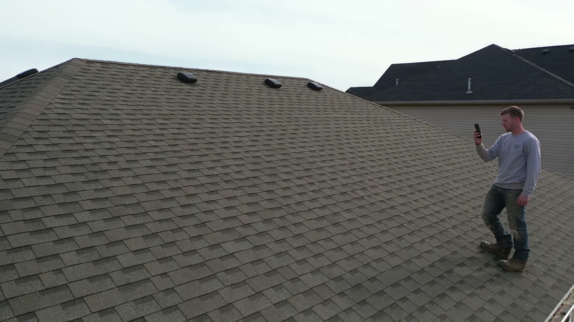 Roofer sa bubong na shingle na kumukuha ng larawan ng trabahong beripikado ng GeoCliks.